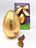 Milk Chocolate Easter Egg in goldr foil with a boxed easter egg in the background and two chunks of milk chocolate cinder toffee in the foreground.  On a white background.