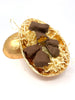 Open milk Chocolate Easter Egg in gold foil filled with pieces of milk chocolate cinder toffee on cream shredded paper.  On a white background.