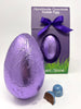 Milk Sea Salt Caramel Easter Egg in purple foil. Gorvett & Stone box in the background and  two Sea Salt Caramel chocolates in the foreground. White background.