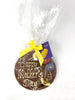 Milk chocolate plaque decorated with Happy Mother's Day, colourful chocolate flowers and a bumble bee. Wrapped in cellophane and tied with a satin ribbon and gift tag. On a white background with pink flowers and a gift card in the background.