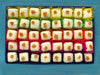 Open gift box of 40 white chocolates decorated with candied orange pieces. Each chocolate is contained in a colourful petits fours case. View from above on a painted blue background.
