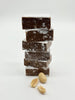 Stack of square peanut butter meltaways dusted with icing sugar. 3 peanuts scattered in front of meltaways. On a white background. 