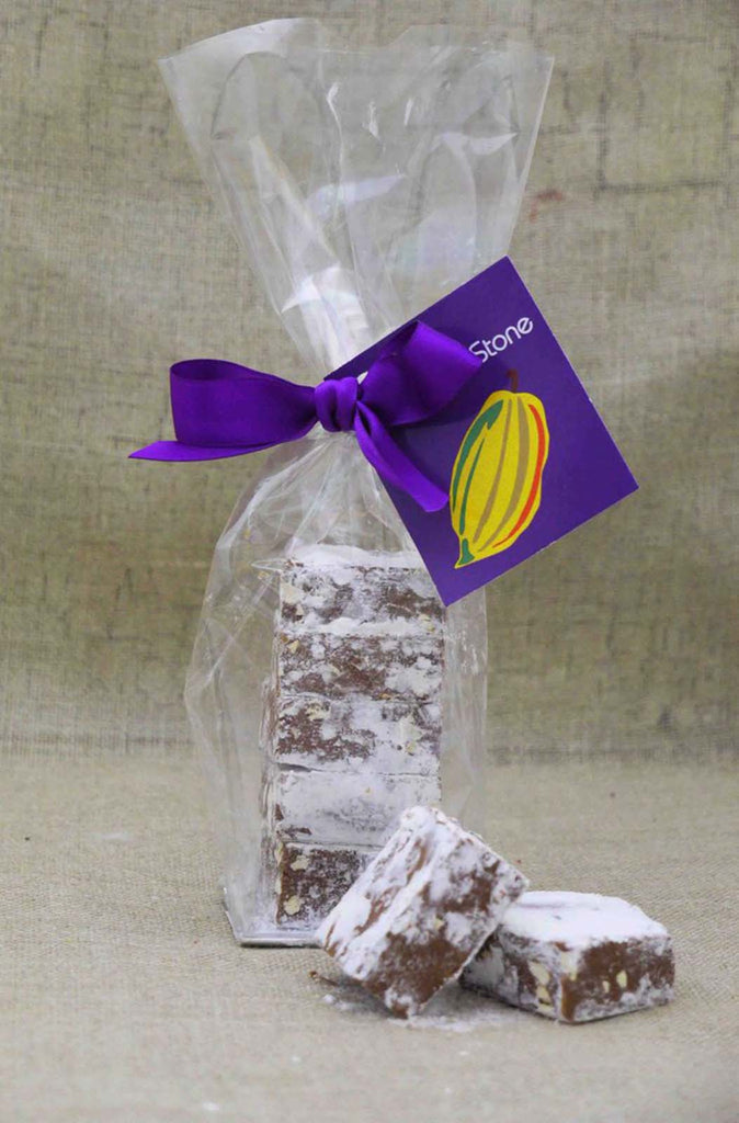 Clear bag filled with peanut butter meltaways. 2 meltaway squares placed in front of the bag. Bag is tied with a ribbon and tag on a beige cloth background.