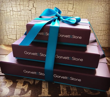 Pyramid of three Gorvett & Stone gift boxes tied with a blue satin ribbon.