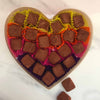 A heart-shaped box containing multiple milk chocolate truffles with sea salt, each dusted with cocoa powder and arranged in colorful paper cases.