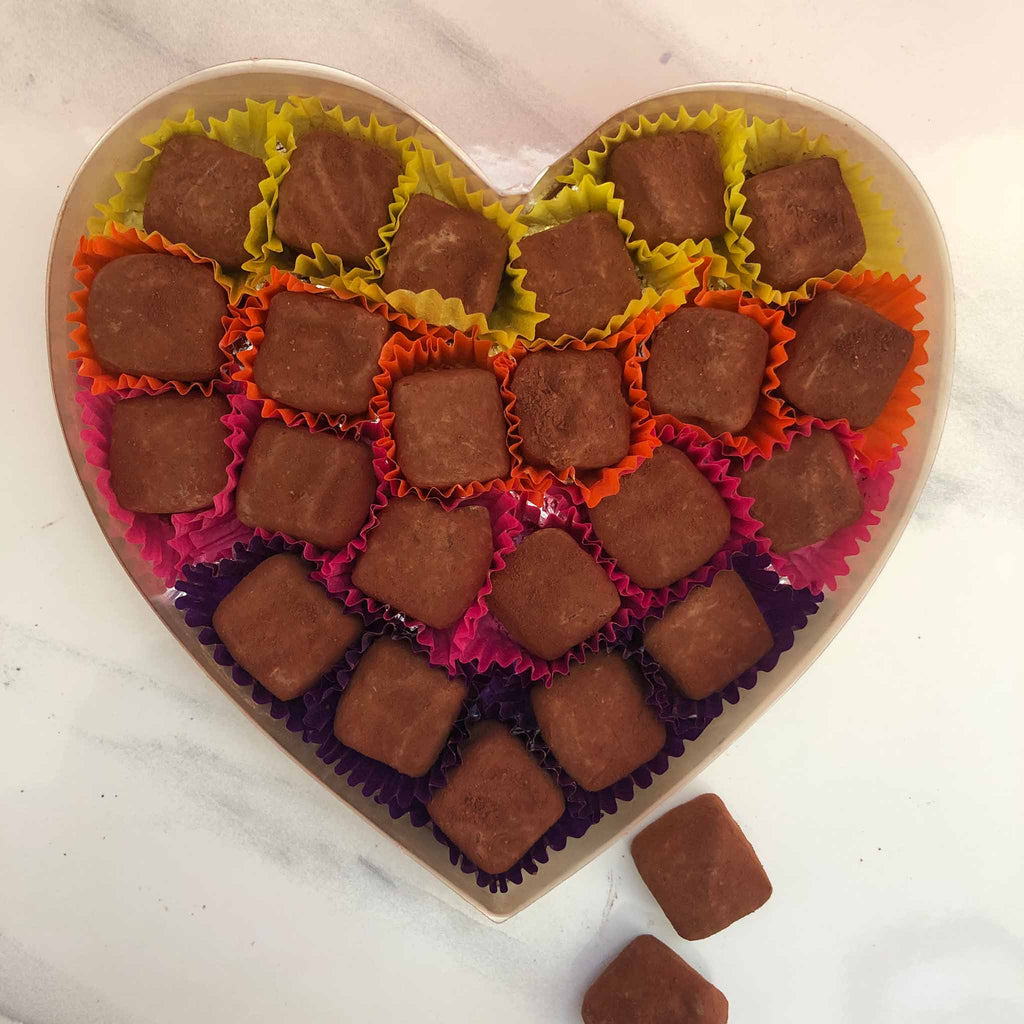 A heart-shaped box containing multiple milk chocolate truffles with sea salt, each dusted with cocoa powder and arranged in colorful paper cases.