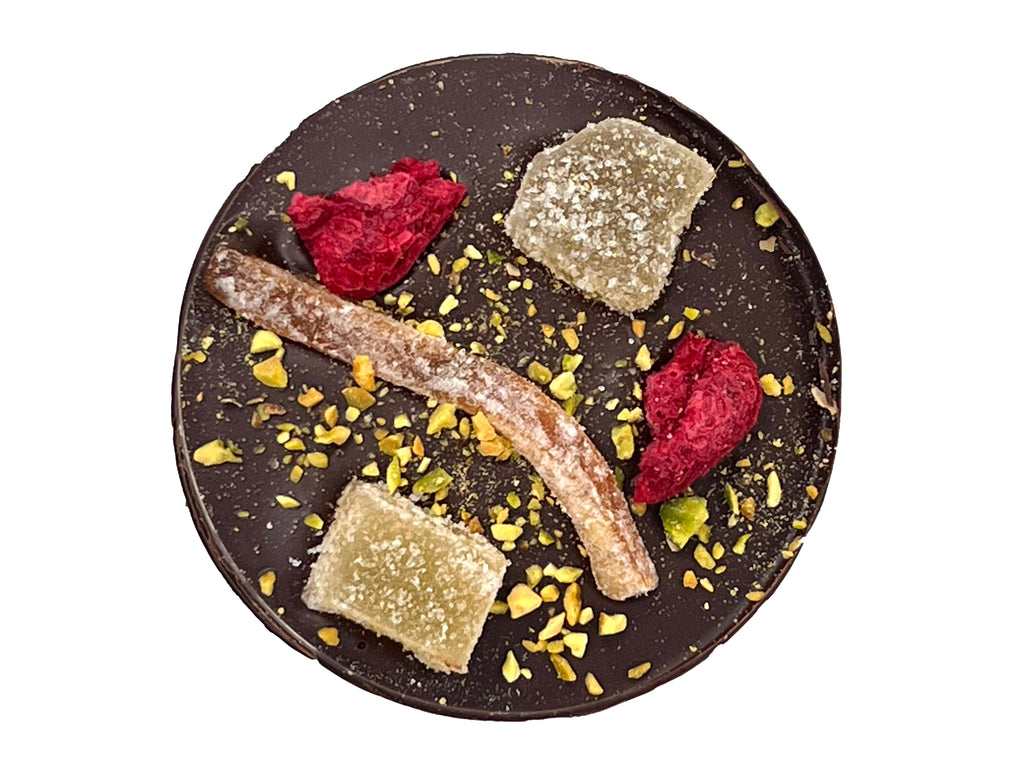 Single dark chocolate giant mendiant topped with raspberry, stem ginger, candied orange and pistachio nuts. View from top down on a white background