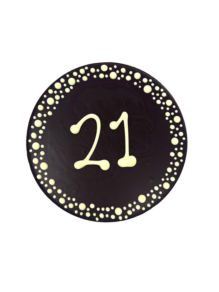 Dark chocolate plaque hand piped  with a decorative border and '21' text in white chocolate. On a white background.
