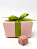 Pink gift box with a green ribbon and a pink chocolate truffle on a white background