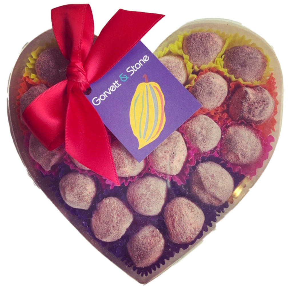 Pink Strawberry Gin Fizz Truffles in a heart shaped box with a clear lid and a red bow.
