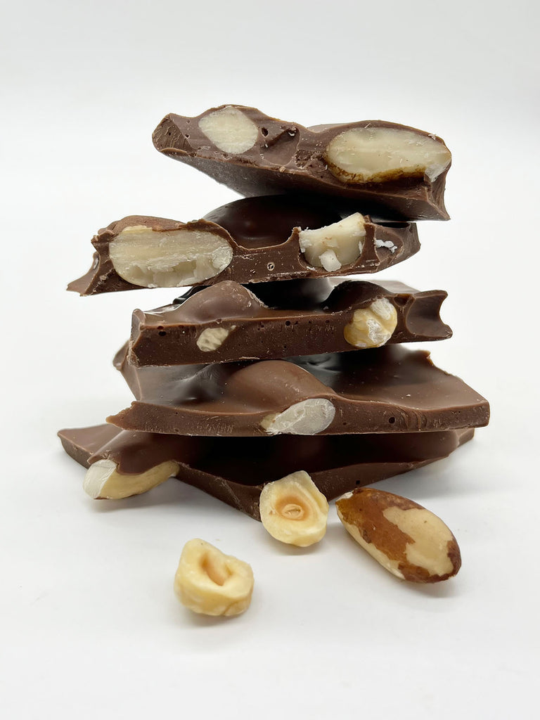Stack of Very Nutty milk chocolate shards with brazil nut and hazelnuts scattered in front.  On a white background.