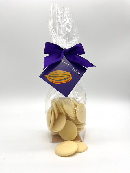 White chocolate couverture buttons in a clear bag. Tied with a purple ribbon and a tag. On a white background.