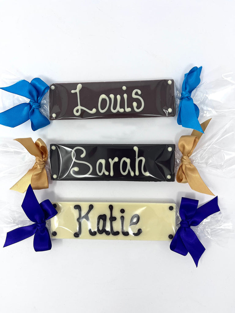 Three chocolate bars with names piped on. Wrapped in cellophane and tied with satin ribbon at each end. On a white background.