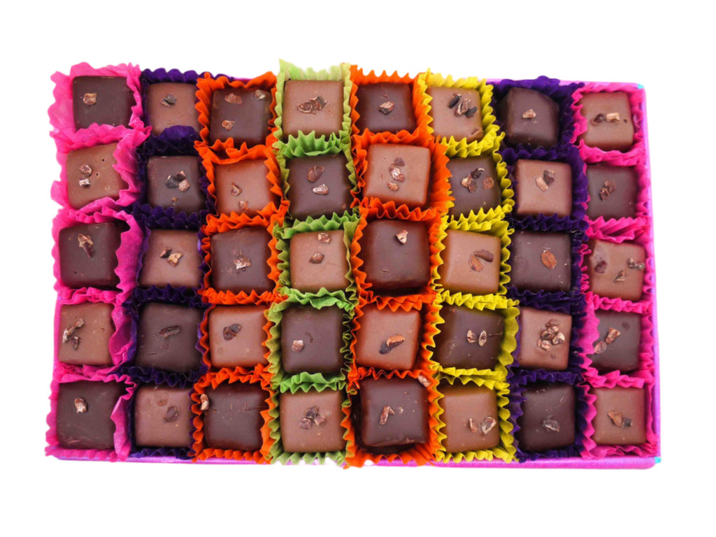 Open gift box of 40 dark and milk chocolates. Pictured in a chequerboard design and each chocolate sitting in a colourful petit four case. Pictured from above on a white background.