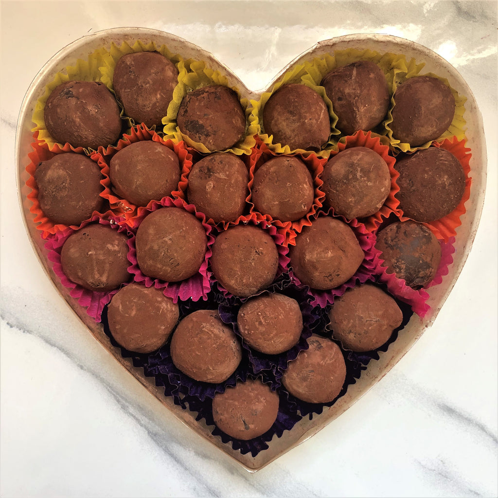 A heart-shaped box containing multiple dark chocolate truffles with cocoa powder dusted on top, displayed on a marble surface.